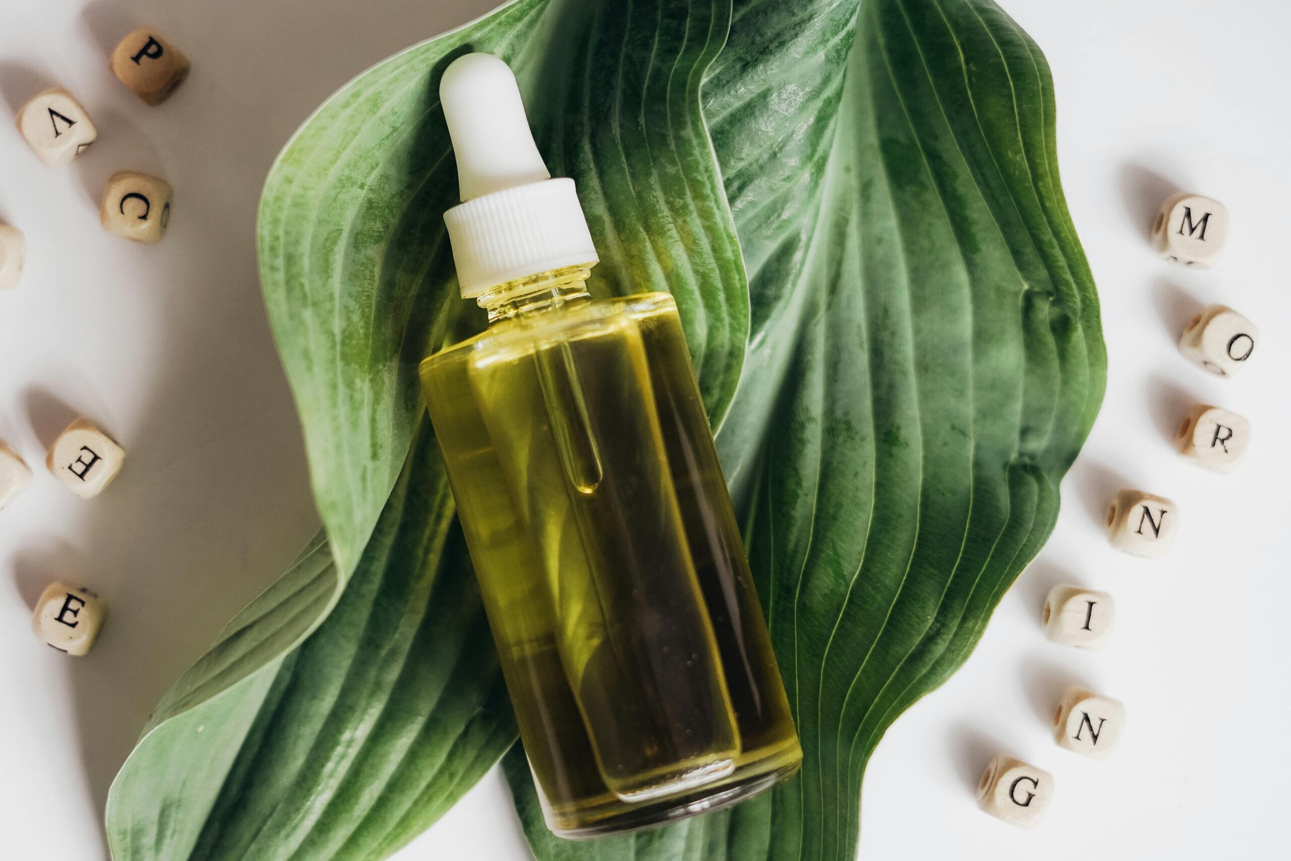 A bottle of natural skincare oil placed on green leaves with letter blocks spelling out 'morning'.