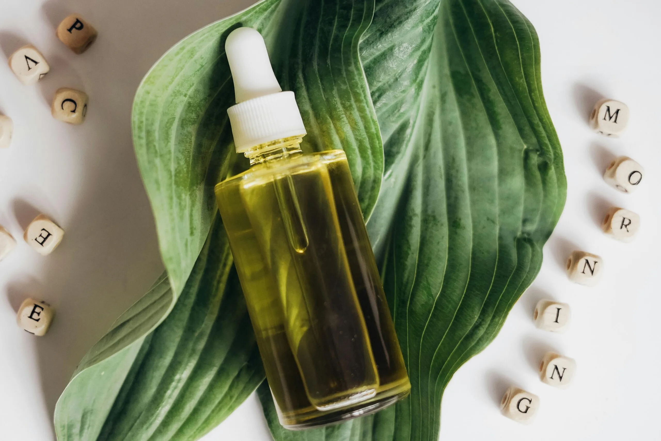 A bottle of natural skincare oil placed on green leaves with letter blocks spelling out 'morning'.